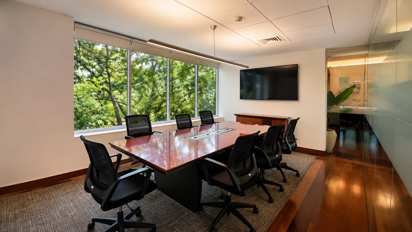 Sala de reunión formal con mesa de directorio, pantalla y vista al parque