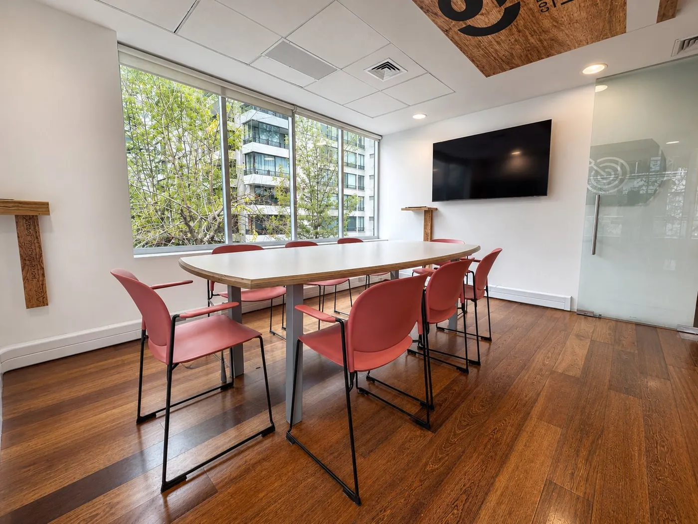 Sala de reunión con mesa ovalada, sillas coral y vista al entorno verde